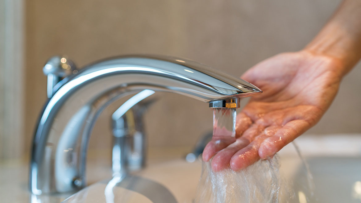 Hands touching running water from faucet.
